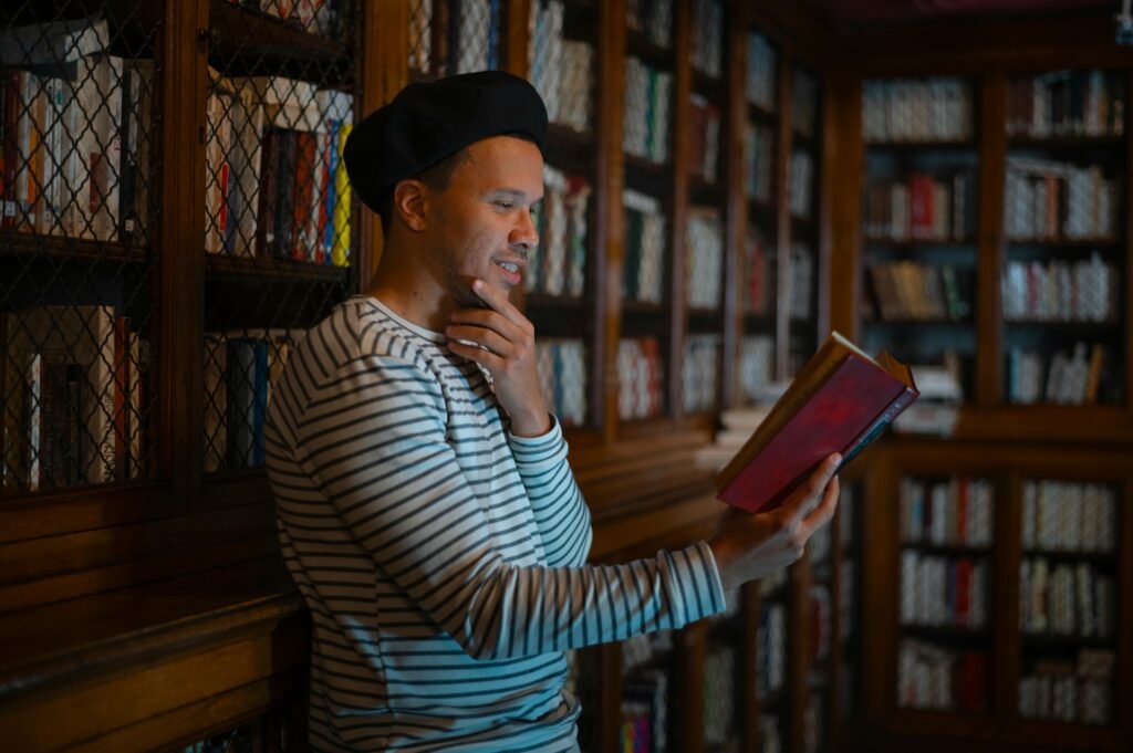 A man enjoys reading in a cozy library with wooden bookshelves, creating a reflective ambiance.